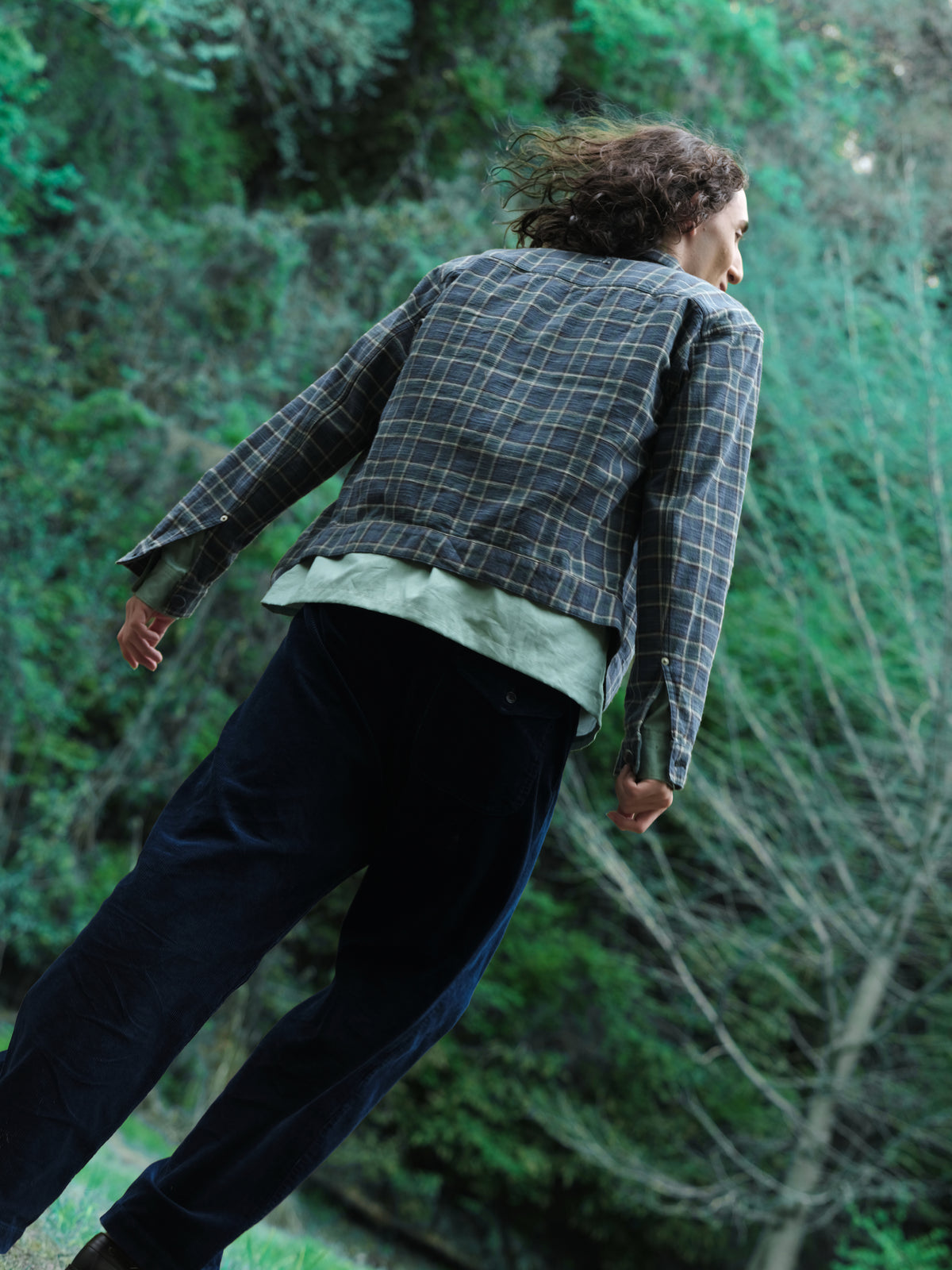 Little Yarmouth EP. 2. The back of a checked jacket and dark trousers against turquoise woodland.
