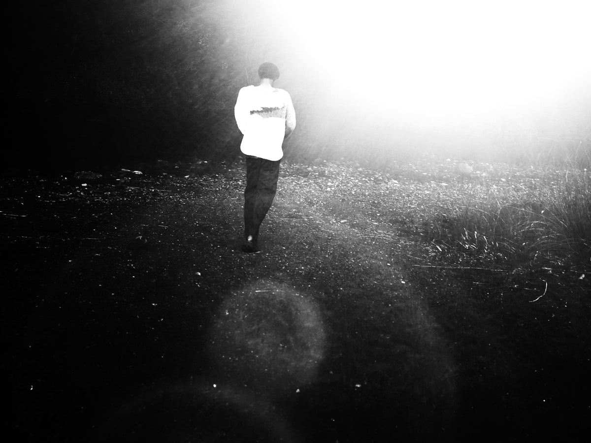 Little Yarmouth EP. 2. A rear view of a figure walking toward a bright light, in black and white.