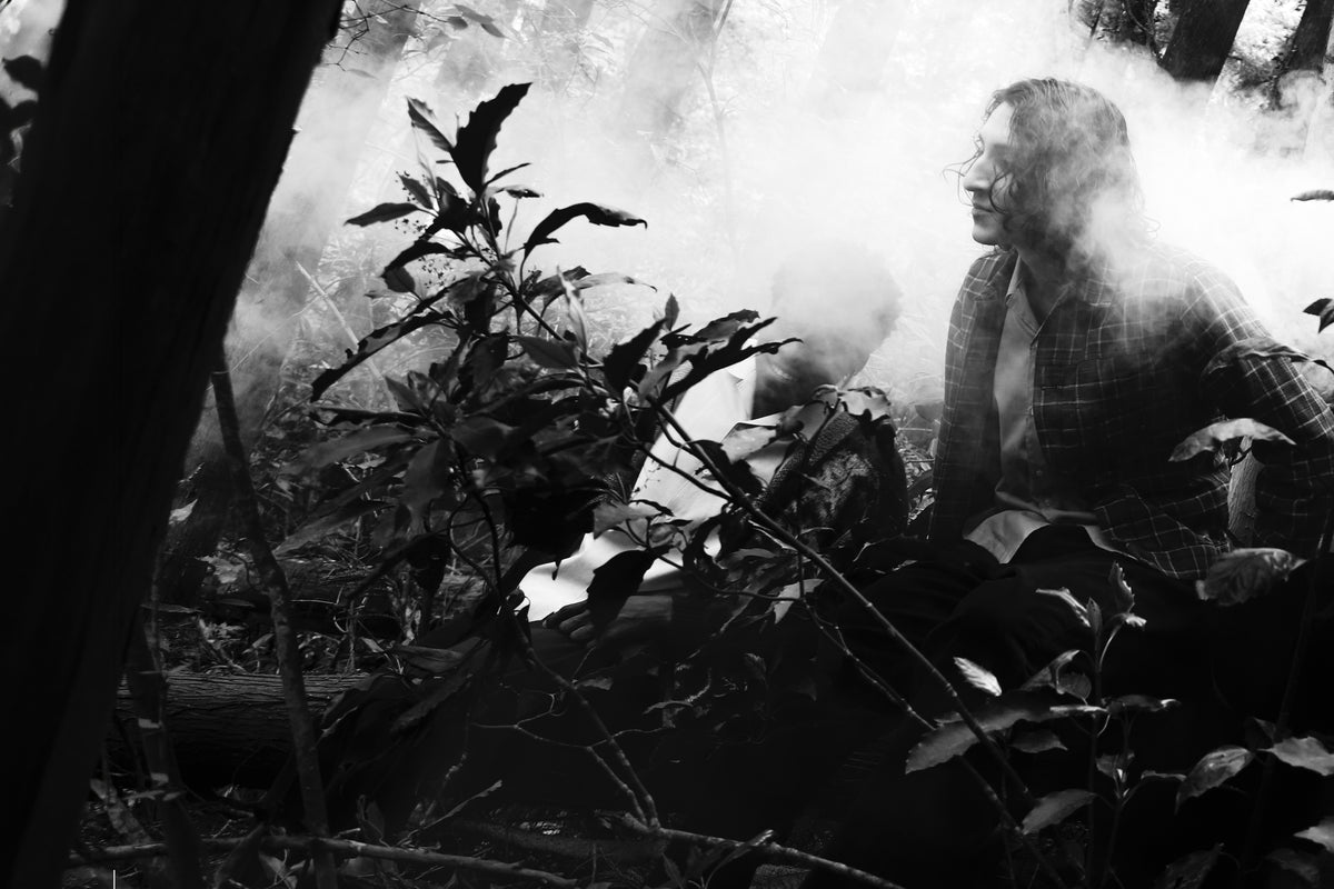 Little Yarmouth EP. 2. A monochrome figure in a misty forest, framed by leaves and sunlight.