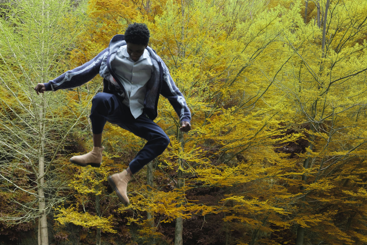 Little Yarmouth EP. 2. A figure leaping in a silver shirt and dark trousers against golden trees.