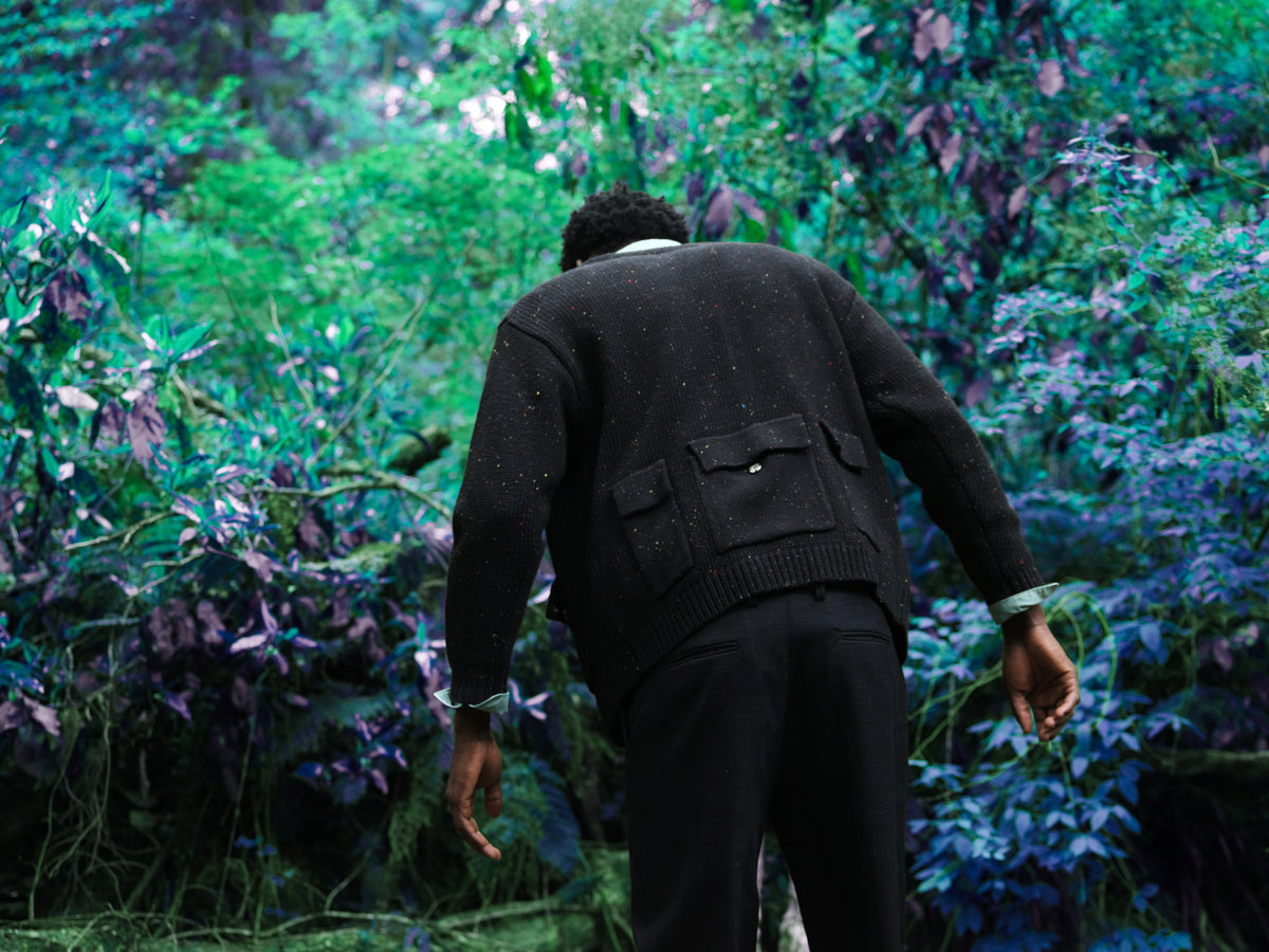 Little Yarmouth EP. 2. A dark cardigan seen from behind amid green and violet foliage.