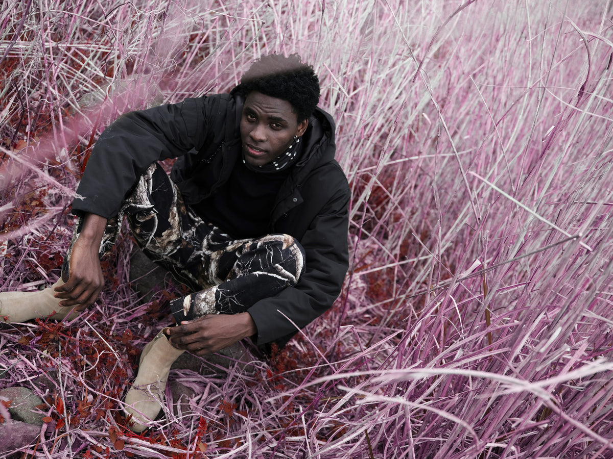 Little Yarmouth EP. 2. A seated figure in patterned trousers among pale purple branches.