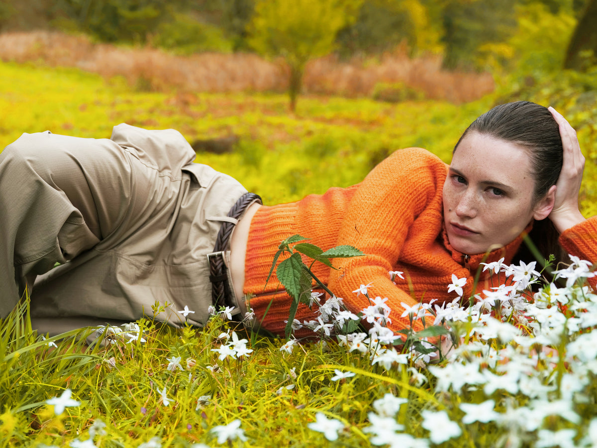 Little Yarmouth EP. 2. A reclining figure in an orange knit and beige trousers in a golden meadow.
