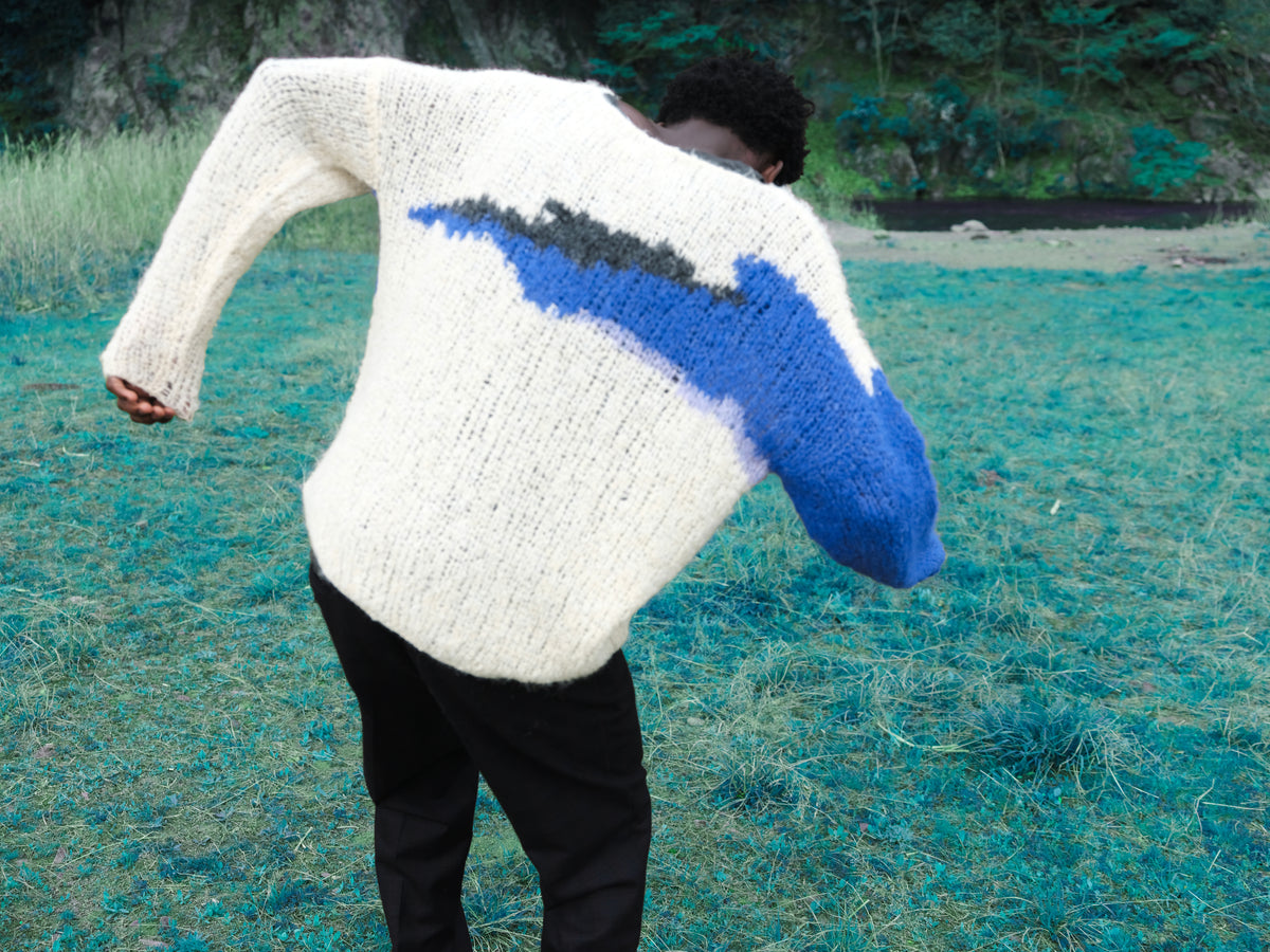 Little Yarmouth EP. 2. A white and blue knit seen from behind in a turquoise meadow.